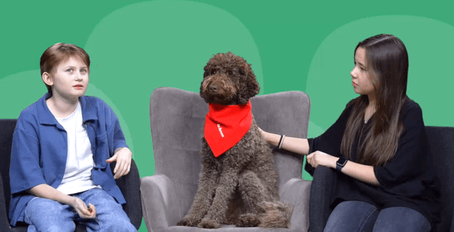 Två barn pratar i en soffa med en hund mellan sig.